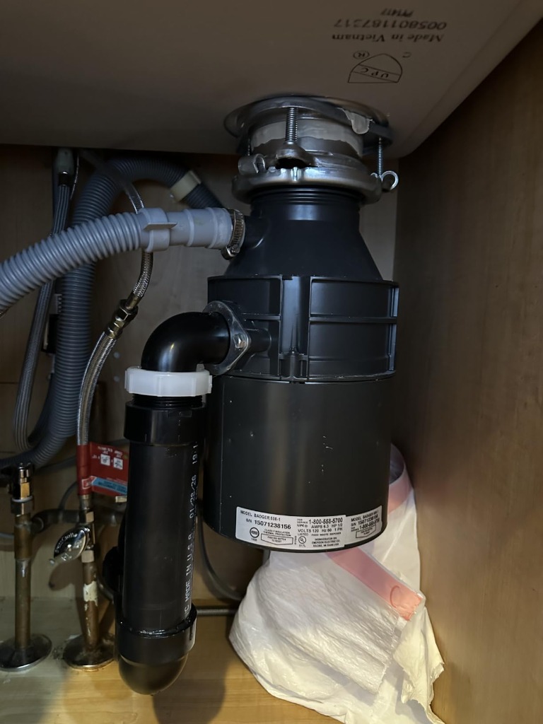 Under-sink plumbing showing InSinkErator garbage disposal connected to the rear offset drain