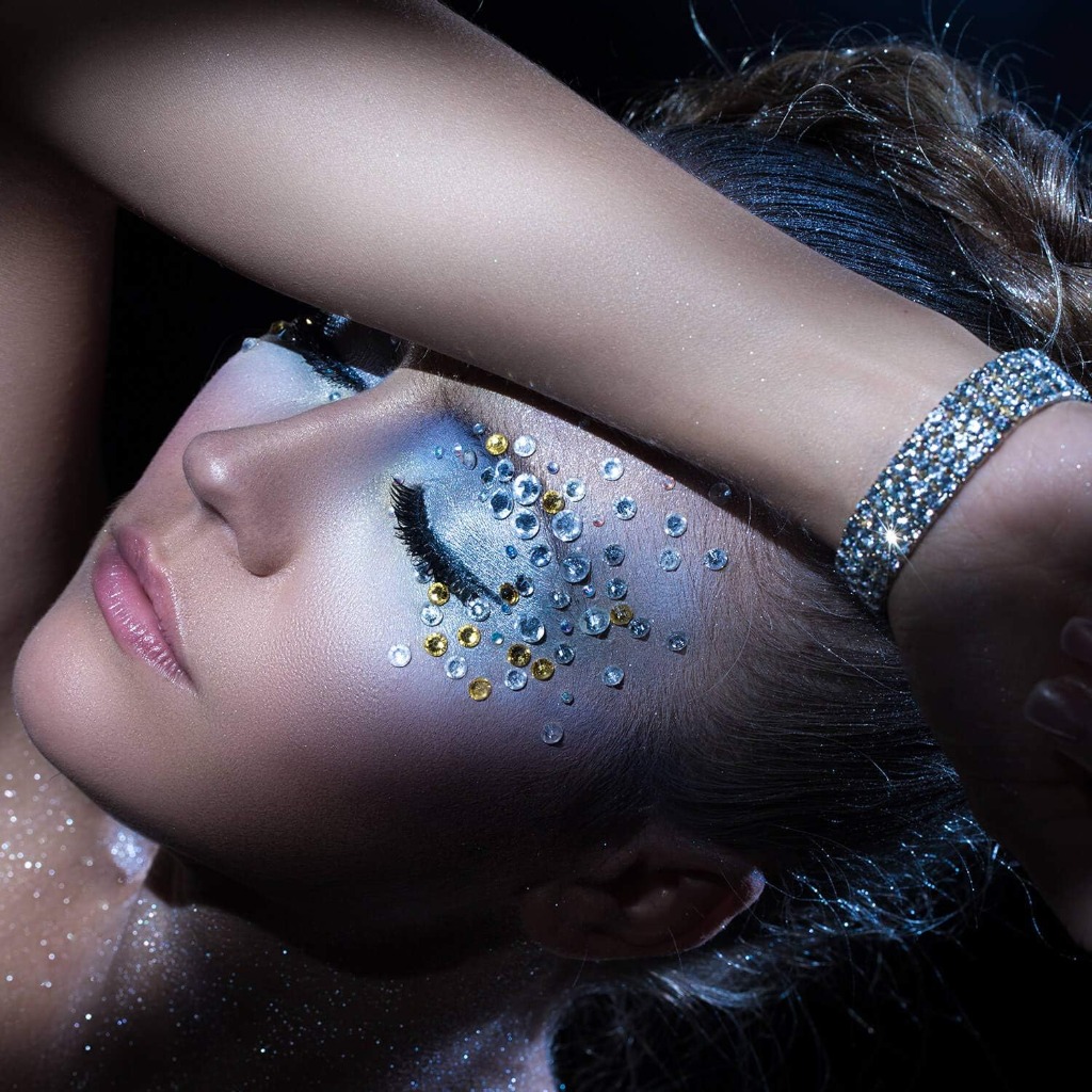 Festival face makeup featuring silver and gold crystal rhinestones catching light on eye and cheekbones