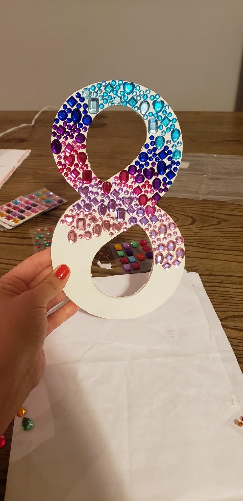 Hand holding painted wooden number 8 decorated with gradient multi-color Selizo rhinestone stickers